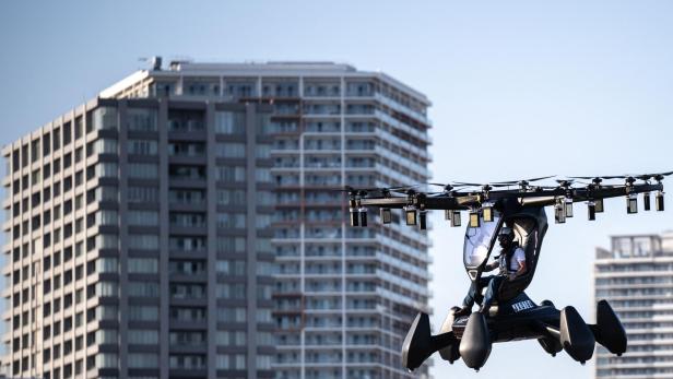 Ein Mann fliegt mit einem elektrischen Senkrechtstarter vor einer Stadtkulisse.