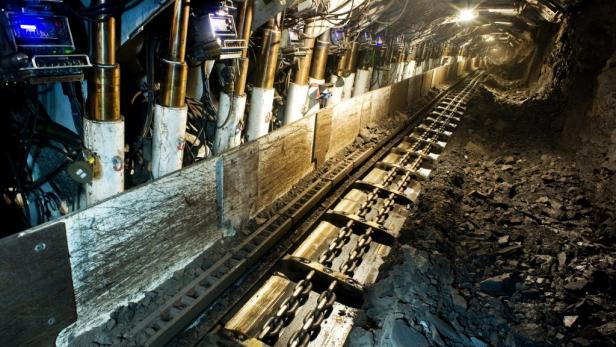 Blick in einen dunklen Kohlebergwerkstollen mit Schienen und Maschinen.