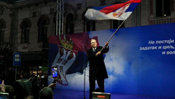 Ein Mann schwenkt eine serbische Flagge vor einer Menschenmenge.