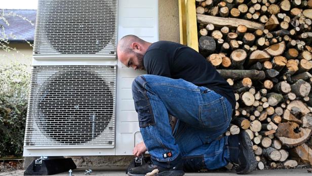 Installateur installiert eine Luft-Wärmepumpe vor einem Haus.