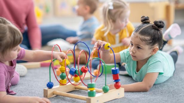 Mehrere Kinder spielen mit einem bunten Motorikspielzeug auf dem Boden.