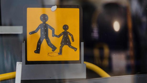 Ein gelbes Schild mit der Silhouette eines Erwachsenen und eines Kindes, die Hand in Hand gehen.