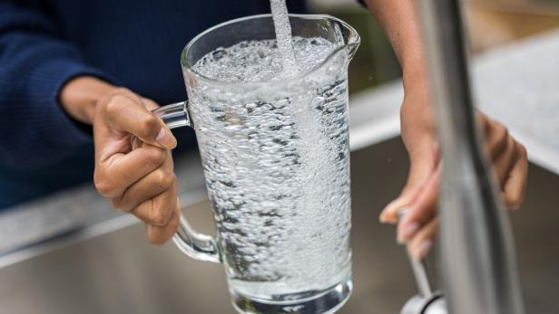 Eine Person füllt einen Glaskrug mit Wasser an einem Wasserhahn.