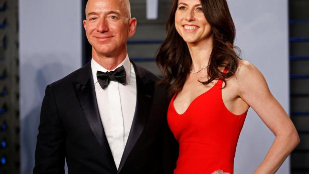 Jeff Bezos im Smoking und MacKenzie Scott in einem roten Kleid lächeln nebeneinander in die Kamera.