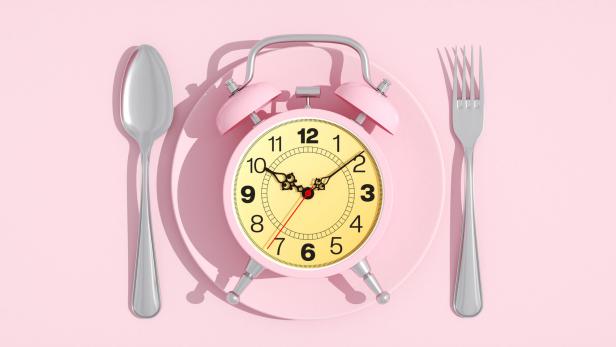 Wecker liegt auf einem Essteller, links und rechts Löffel und Gabel.