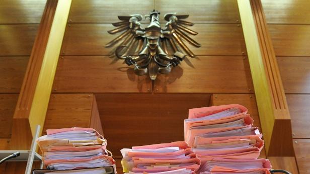 Stapel von Akten mit rosa Deckblättern liegen vor einem hölzernen Richterpult mit dem deutschen Bundesadler im Hintergrund.