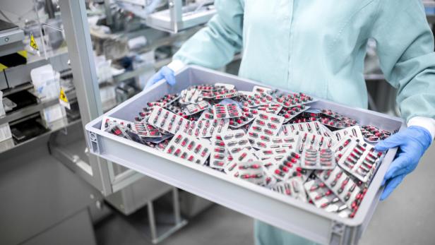 Frau mit Handschuhen trägt ein Tablett mit Tablettenpackungen.