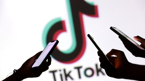 Eine Illustration zeigt Teenager, die mit Smartphones vor einem TikTok-Logo für ein Foto posieren.