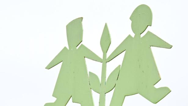 Zwei stilisierte grüne Kinderfiguren halten eine Pflanze auf einem verwitterten Holzschild.