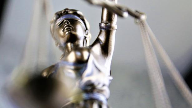 Eine silberne Justitia-Figur mit verbundenen Augen hält eine Waage in der erhobenen Hand.