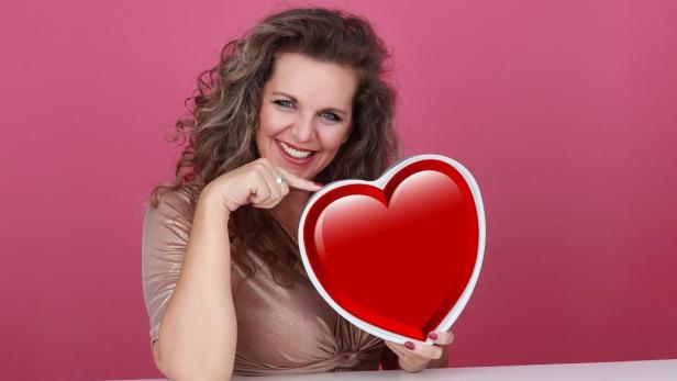 Eine Frau mit einem großen herz in der Hand lächelt in die Kamera