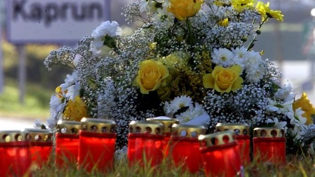 Kerzen und Blumen im Vordergrund, dahinter Ortsschild von Kaprun