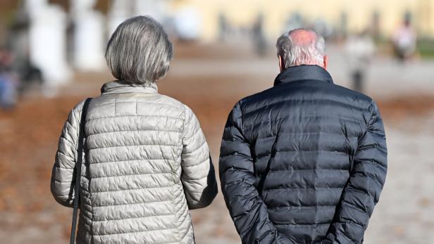 Zwei ältere Personen mit grauen Haaren gehen nebeneinander auf einem Weg, beide tragen Steppjacken.