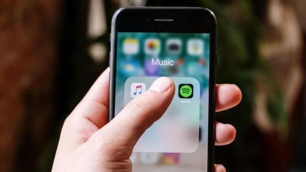Hand hält Smartphone mit geöffnetem Musik-Ordner und sichtbarem Spotify-Icon.