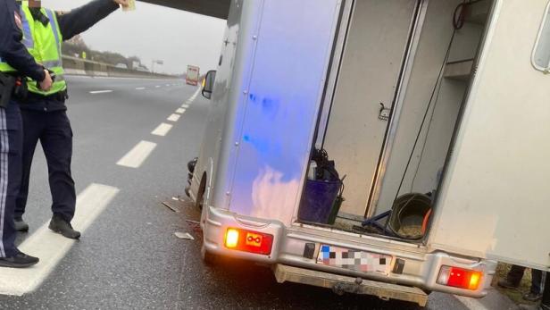 Auf einer Autobahn steht ein beschädigter Pferdeanhänger, während Polizisten die Situation begutachten.