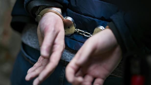 Hände einer Person sind hinter dem Rücken mit Handschellen gefesselt.