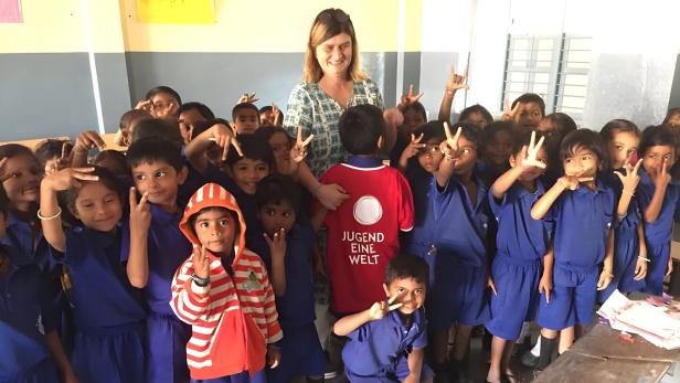 Eine Gruppe Kinder in blauen Schuluniformen posiert mit einer Frau und einem Jungen mit "Jugend Eine Welt"-Shirt.