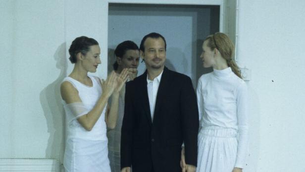 Mann im dunklen Anzug, umstellt von Frauen in weißen Kleidern