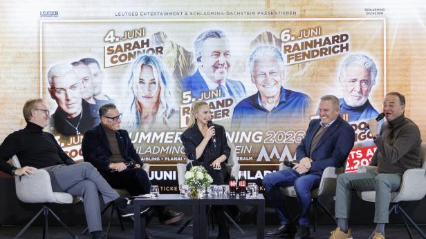 Vier Männer und eine Frau sitzen auf Bühne vor Plakat