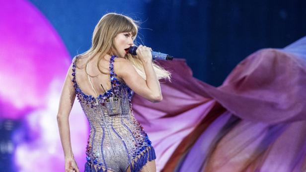 Taylor Swift singt in einem glitzernden, blau verzierten Bühnenoutfit ins Mikrofon.