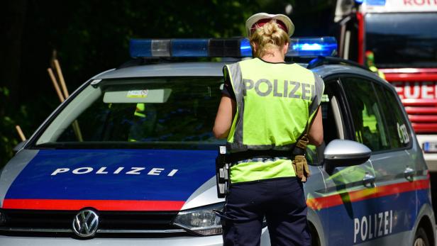 Eine Polizistin steht vor einem Polizeiauto mit eingeschaltetem Blaulicht und trägt eine Warnweste.