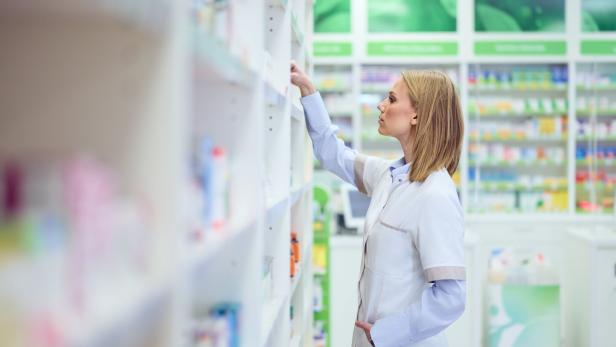 Professional Pharmacist Arranging Medicine Shelves Inside a Modern Pharmacy Store