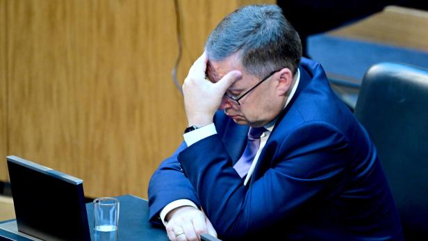 August Wöginger sitzt mit gesenktem Kopf und gestützt auf die Hand an einem Tisch.