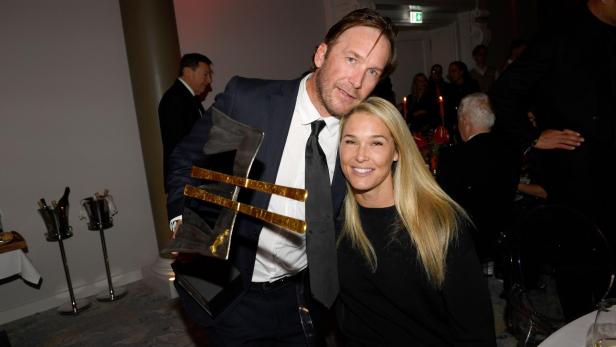 Ein Mann mit einem Award in der Hand kuschelt sich an seine Ehefrau