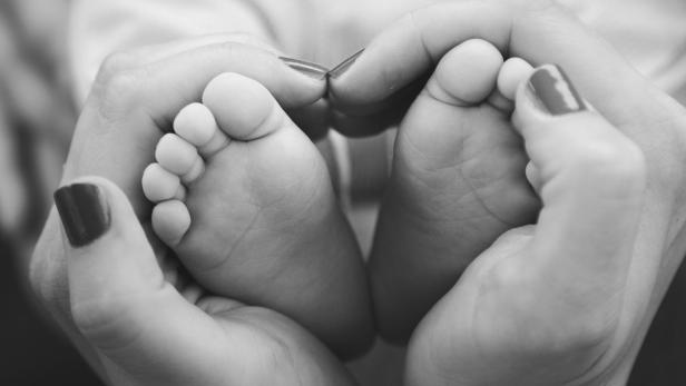 Schwarzweißfoto einer Frauenhand, die Babyfüße in Händen hält