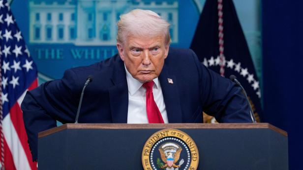 Donald Trump steht mit ernstem Blick hinter einem Rednerpult mit dem Siegel des Präsidenten.