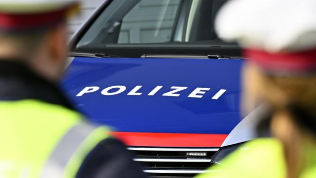 Zwei Polizisten stehen vor einem Polizeiauto mit blau-roter Motorhaube und dem Schriftzug „Polizei“.