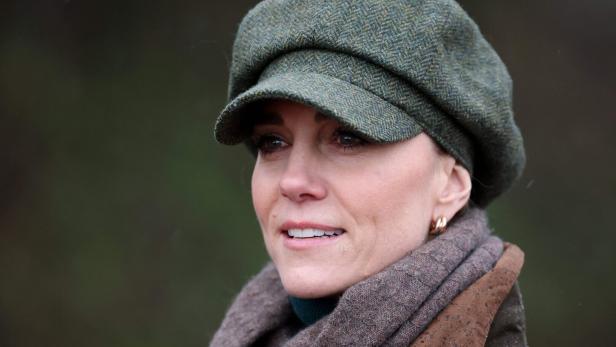 Prinzessin Kate mit grünem Schirmmütze und braunem Schal blickt lächelnd nach vorn.