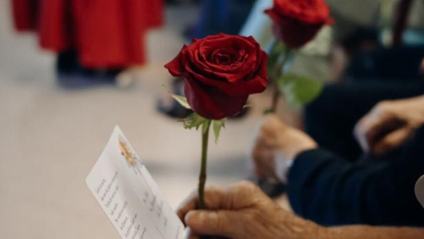 Eine ältere Hand hält eine Rose und eine Karte