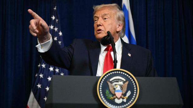 Donald Trump gestikuliert an einem Rednerpult mit dem US-amerikanischen Wappen.