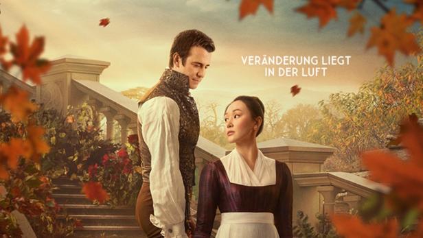 Luke Thompson und Yerin Ha in ihren Serienrollen auf einer Treppe unter rotem Laub