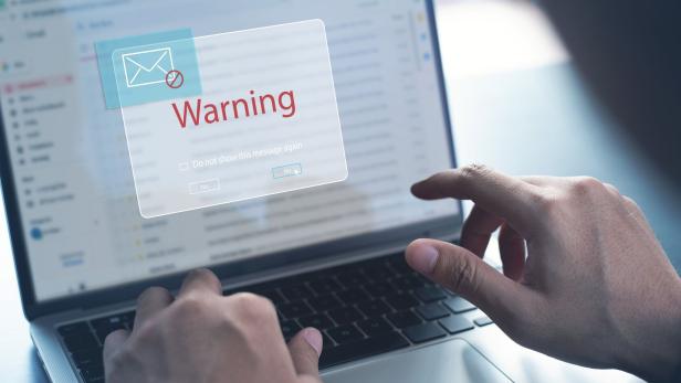 Eine Person arbeitet am Laptop, während eine große Warnmeldung mit einem Briefsymbol auf dem Bildschirm erscheint.