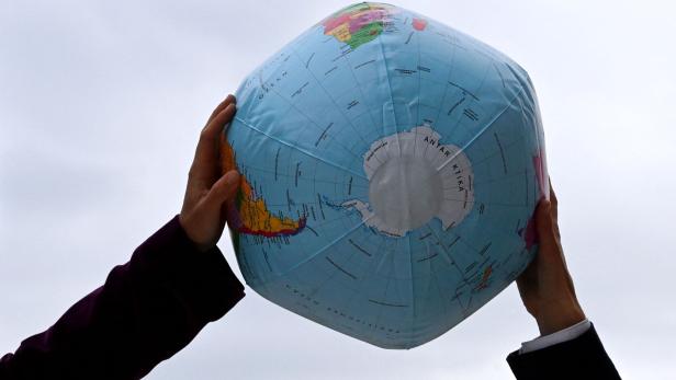 Zwei Hände halten einen aufblasbaren Globus mit der Antarktis nach oben.