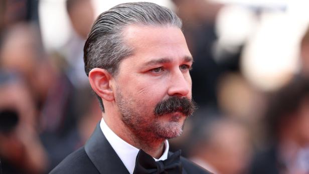 Shia LaBeouf mit zurückgekämmtem Haar und Schnurrbart trägt einen Smoking mit Fliege.