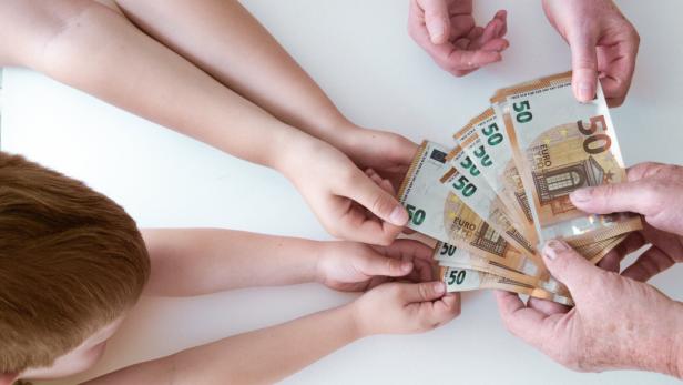 Ein Kind und eine ältere Person halten gemeinsam einen Fächer aus 50-Euro-Scheinen.