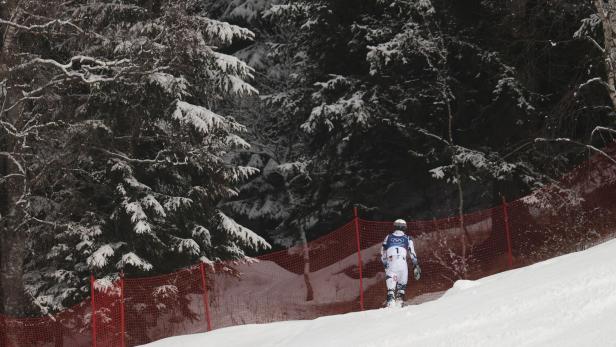 Ein Skifahrer in Rennanzug steht vor einem roten Sicherheitsnetz im verschneiten Wald.