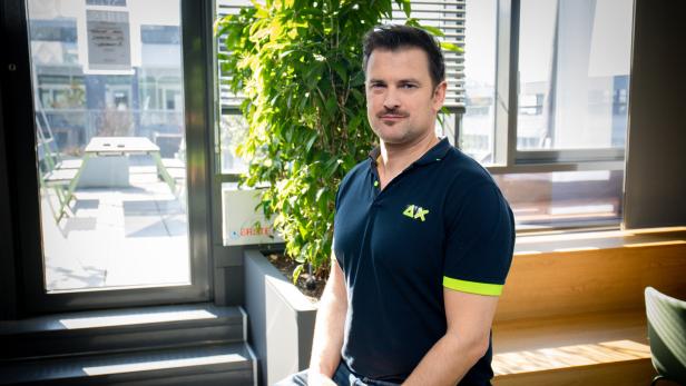 Ein Mann sitzt in einem modernen, sonnendurchfluteten Raum neben einer großen grünen Pflanze.