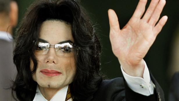 Michael Jackson mit Brille und Anzug winkt in die Kamera.