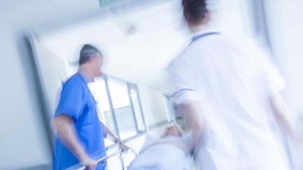 Zwei Pflegekräfte schieben eine Patientin auf einer Trage eilig durch einen Krankenhausflur.