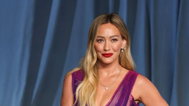 Hilary Duff trägt ein langes, violettes Kleid mit roten Lippen.