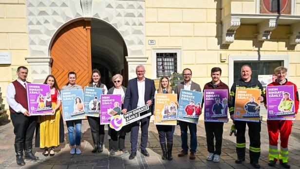 Eine Gruppe von Menschen steht vor einem Gebäude und hält bunte Plakate mit dem Slogan „Mein Einsatz zählt“.