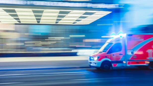 Krankenwagen mit Blaulicht fährt schnell durch eine beleuchtete Stadt bei Nacht.