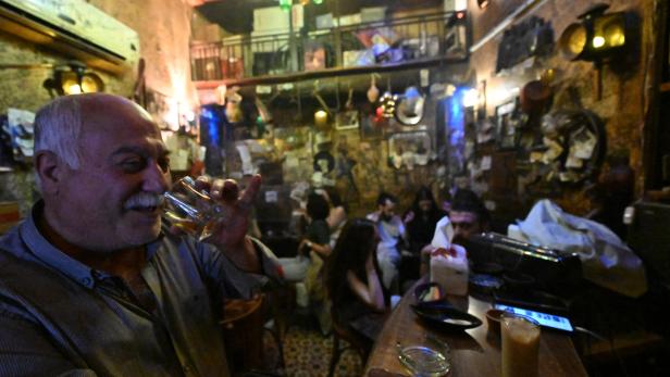Ein älterer Mann trinkt in einer Bar ein Glas.
