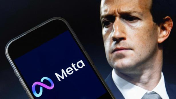 Mark Zuckerberg blickt ernst hinter einem Smartphone hervor, auf dessen Display das Logo von Meta zu sehen ist.