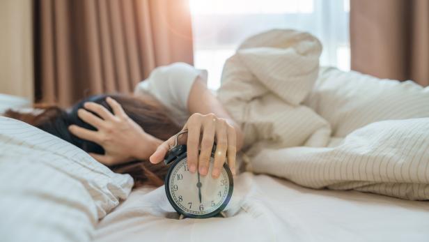 Eine Frau liegt im Bett und schlägt auf ihren Wecker. 