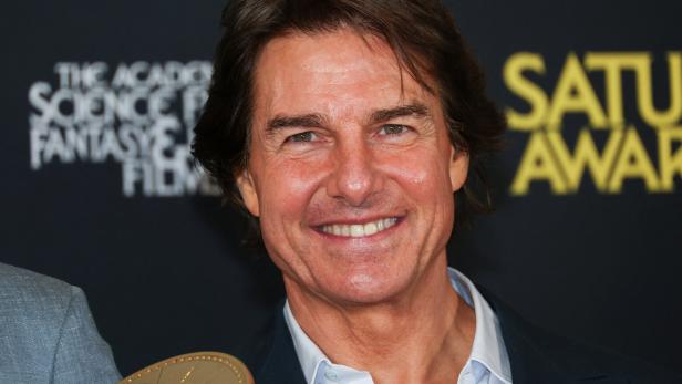 Tom Cruise lächelt vor einem Hintergrund der Saturn Awards.